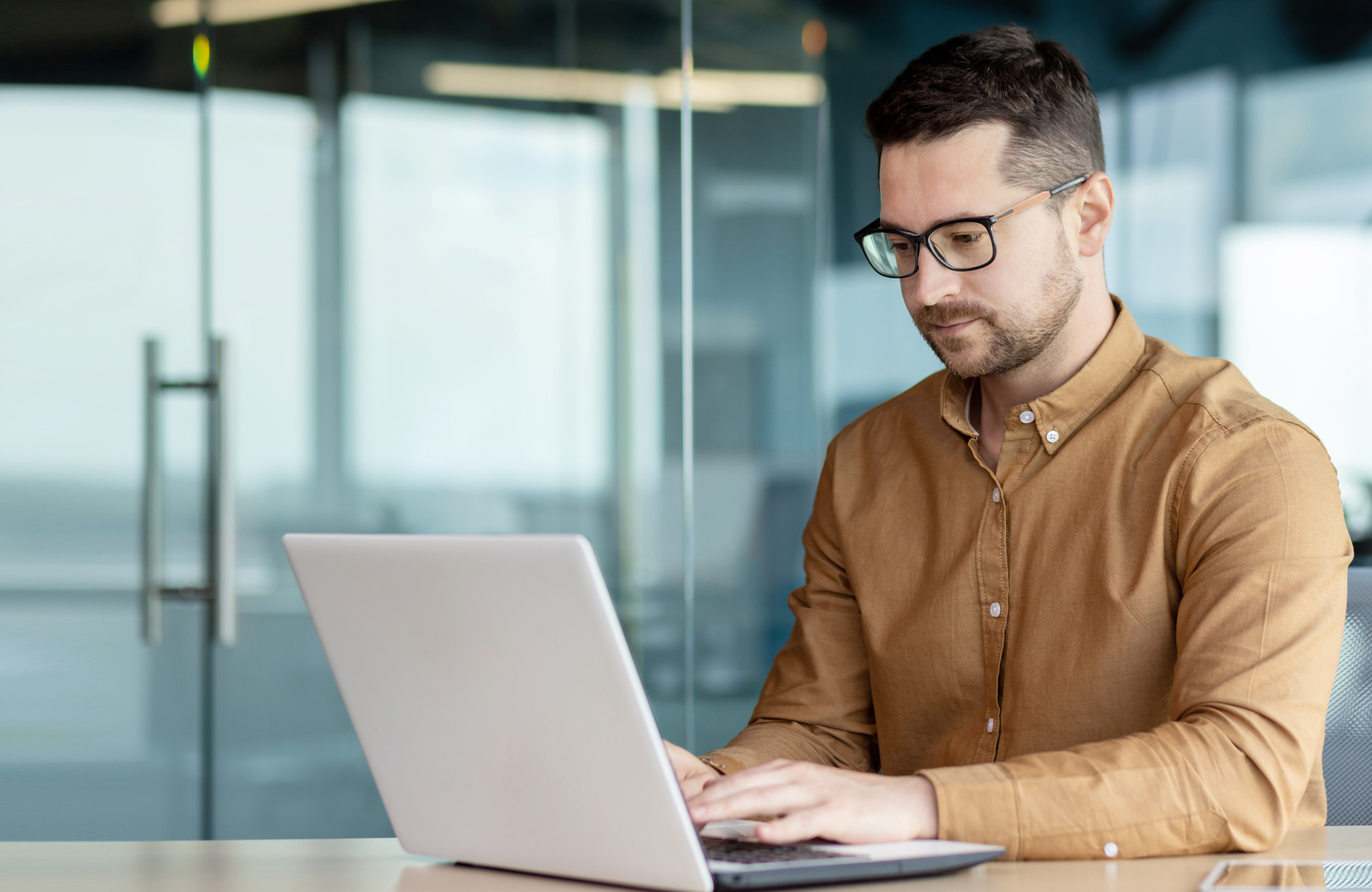 Person working on a laptop in a modern office with glass walls.